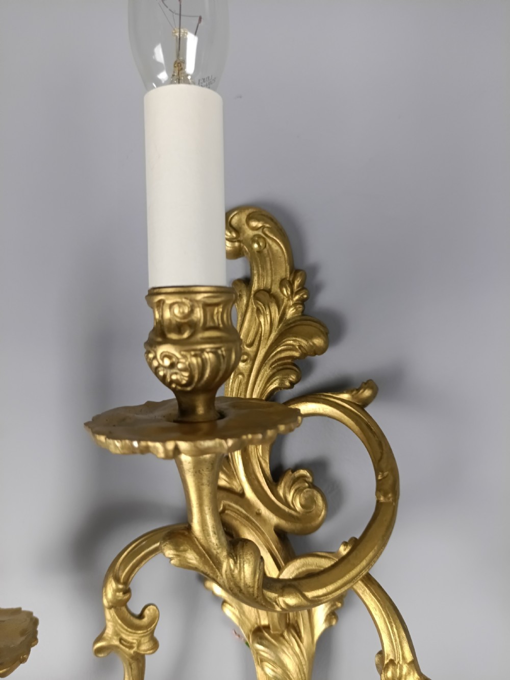 A pair of French Rococo style gilded brass triple arm wall sconces featuring ornate acanthus leaf scrollwork and candle shaped light fittings. View VII