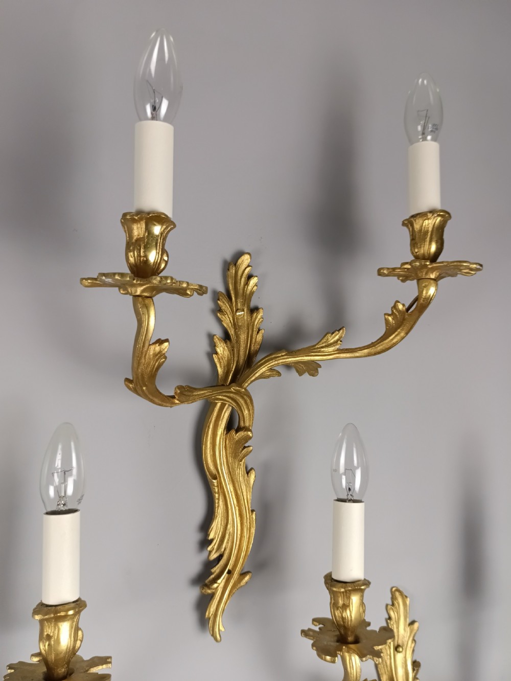A set of four antique French Rococo style gilt bronze wall lights featuring twin curving foliate arms and acanthus leaf backplates. View III