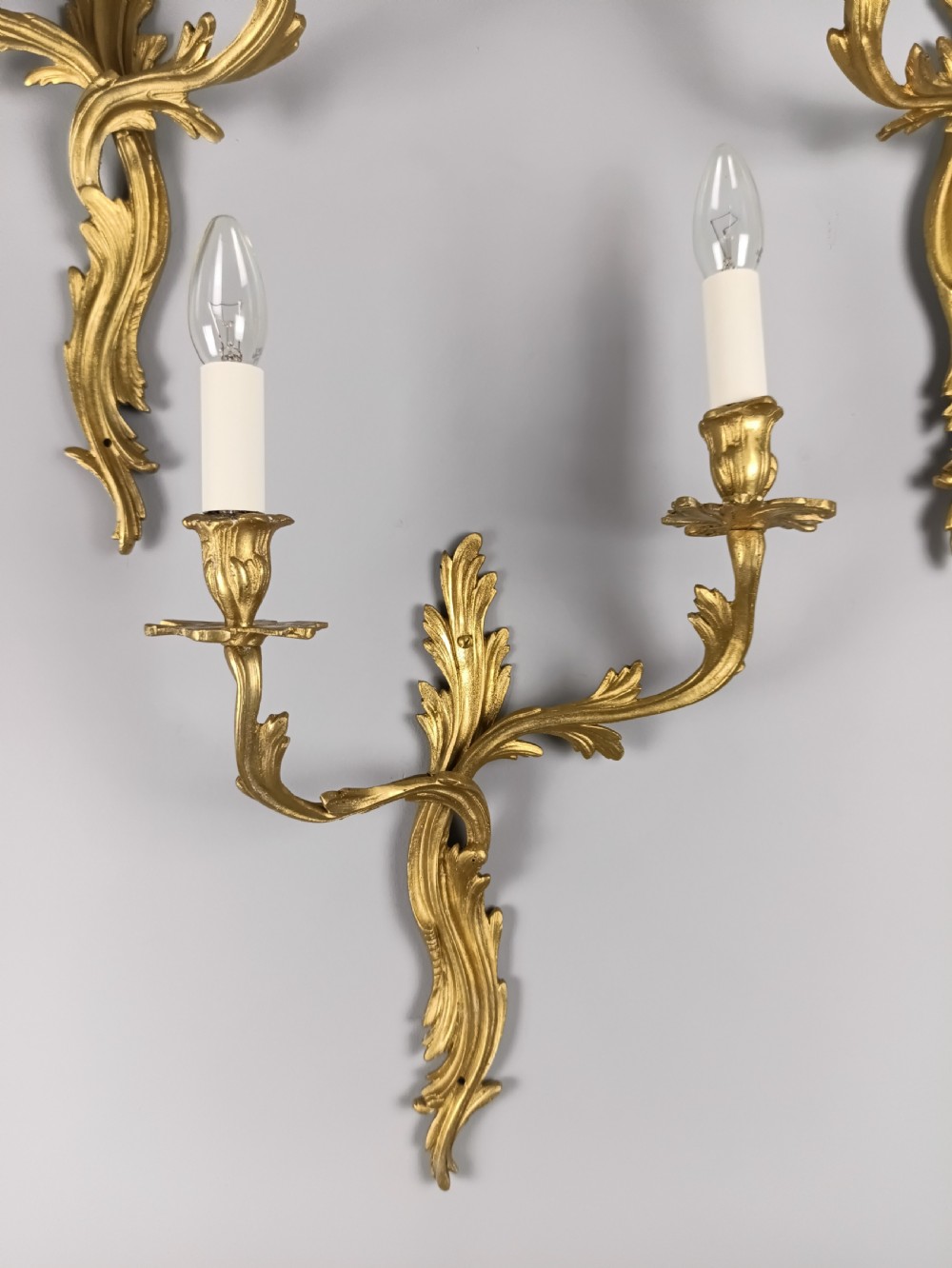 A set of four antique French Rococo style gilt bronze wall lights featuring twin curving foliate arms and acanthus leaf backplates. View V