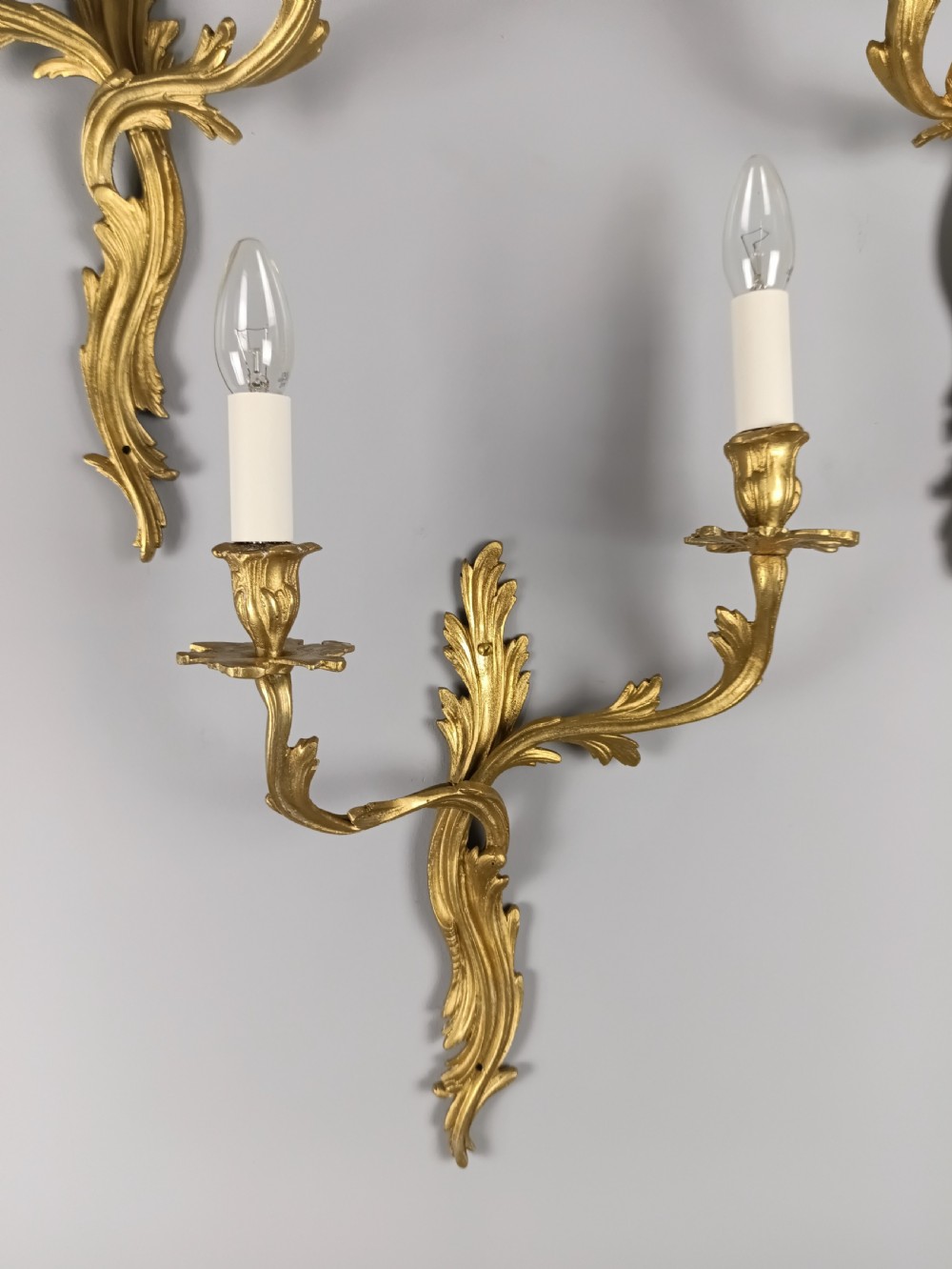 A set of four antique French Rococo style gilt bronze wall lights featuring twin curving foliate arms and acanthus leaf backplates. View VIII