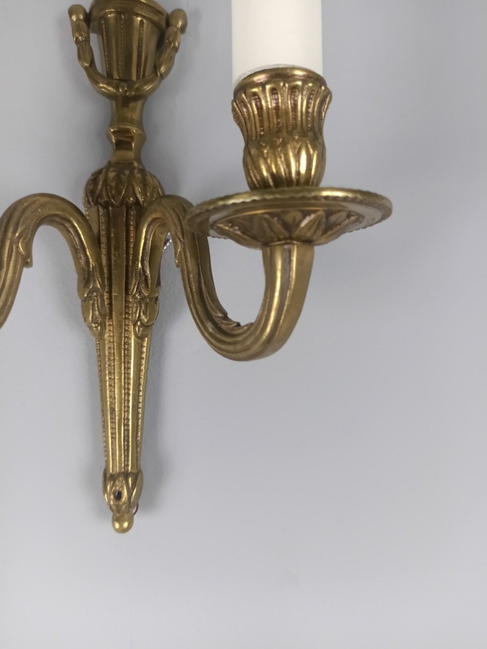 A set of four French antique twin-arm wall lights crafted from gilded brass with neoclassical urn backplates and faux candle sleeves. View II