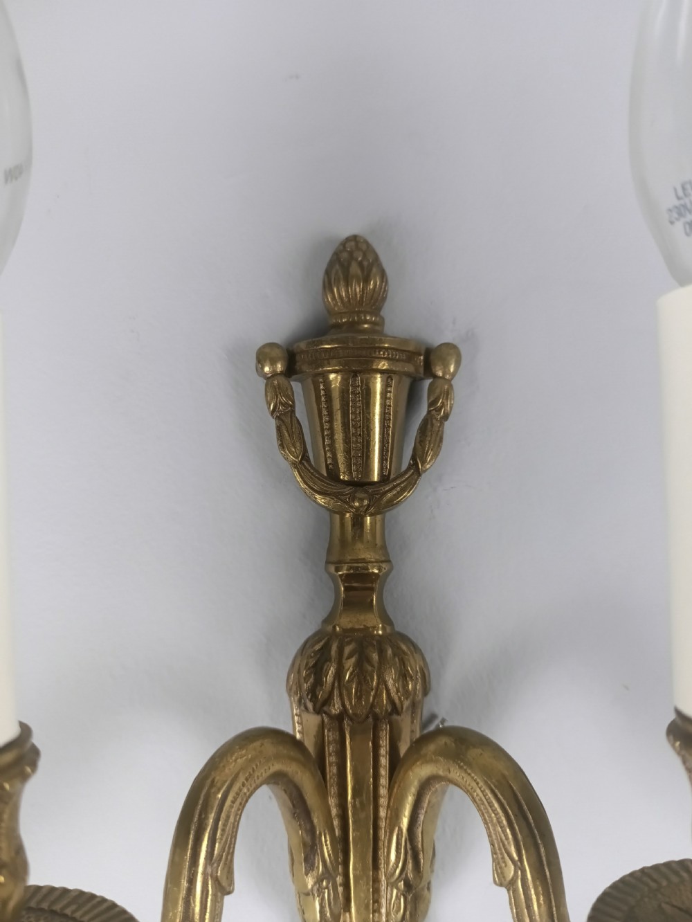 A set of four French antique twin-arm wall lights crafted from gilded brass with neoclassical urn backplates and faux candle sleeves. View III