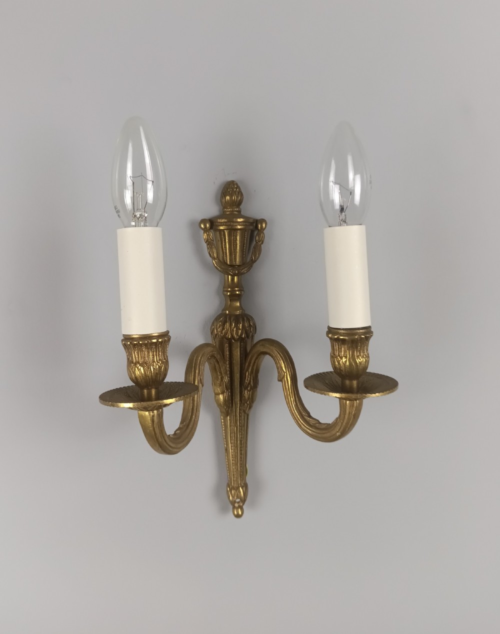 A set of four French antique twin-arm wall lights crafted from gilded brass with neoclassical urn backplates and faux candle sleeves. View IV