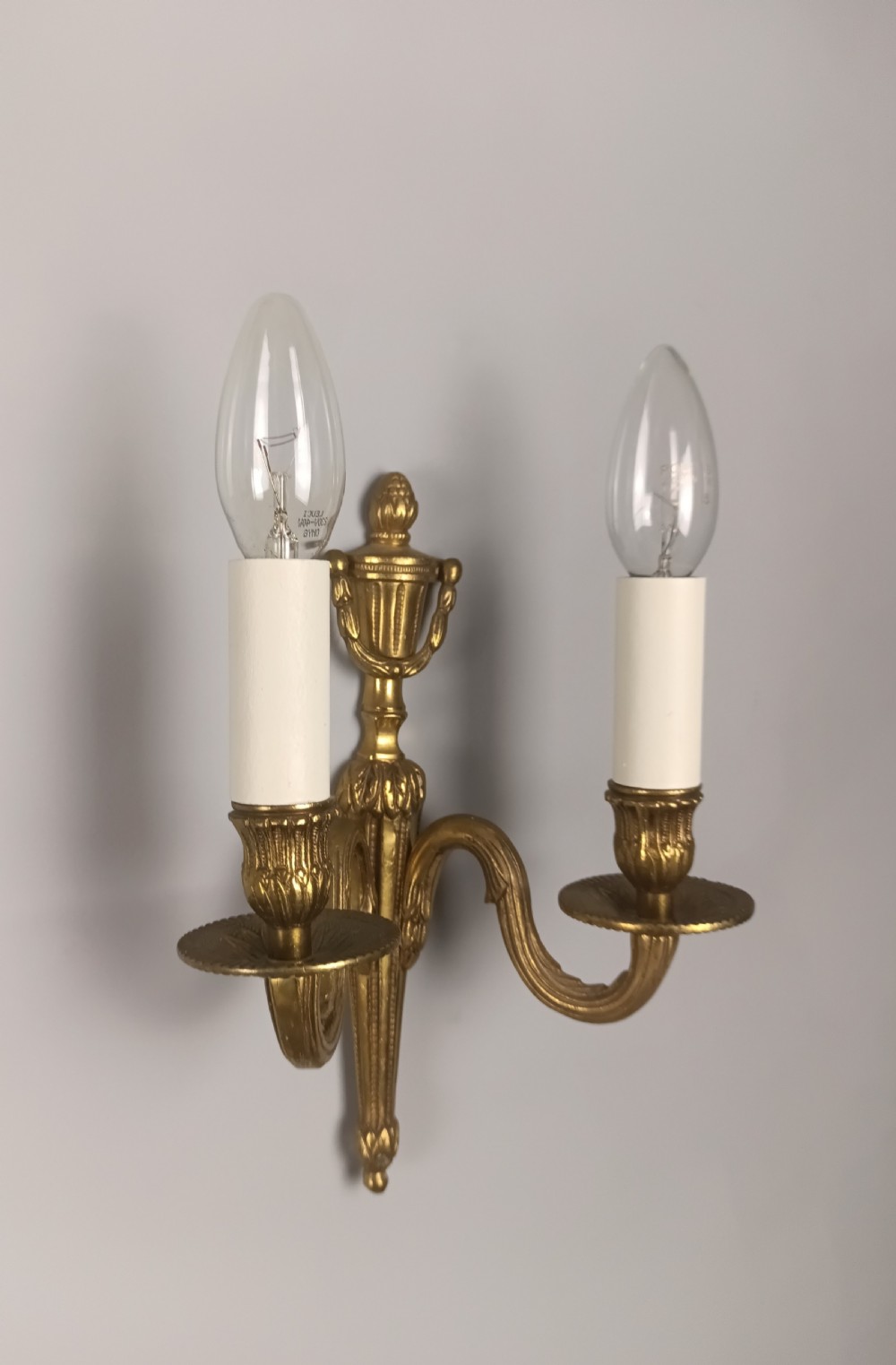 A set of four French antique twin-arm wall lights crafted from gilded brass with neoclassical urn backplates and faux candle sleeves. View VI