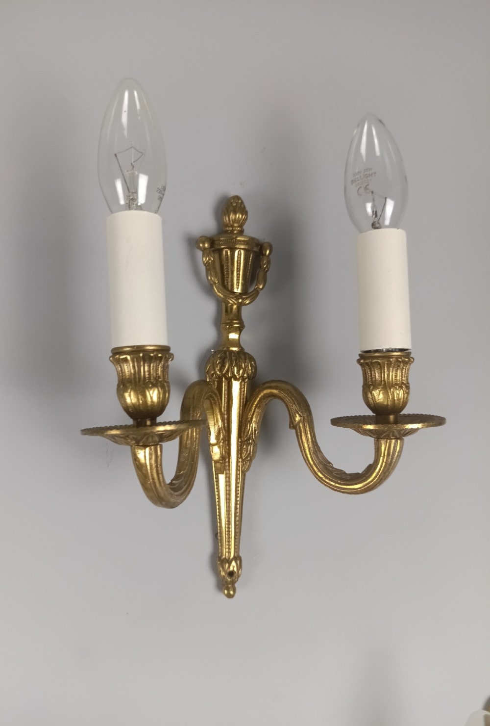 A set of four French antique twin-arm wall lights crafted from gilded brass with neoclassical urn backplates and faux candle sleeves. View VII