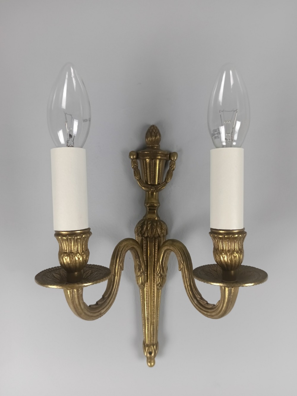 A set of four French antique twin-arm wall lights crafted from gilded brass with neoclassical urn backplates and faux candle sleeves. View VIII