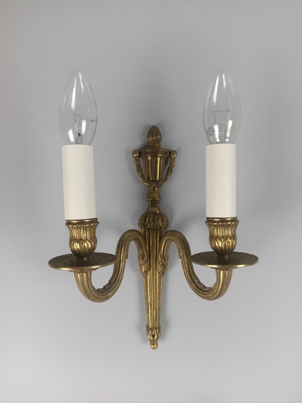 A set of four French antique twin-arm wall lights crafted from gilded brass with neoclassical urn backplates and faux candle sleeves. View IX