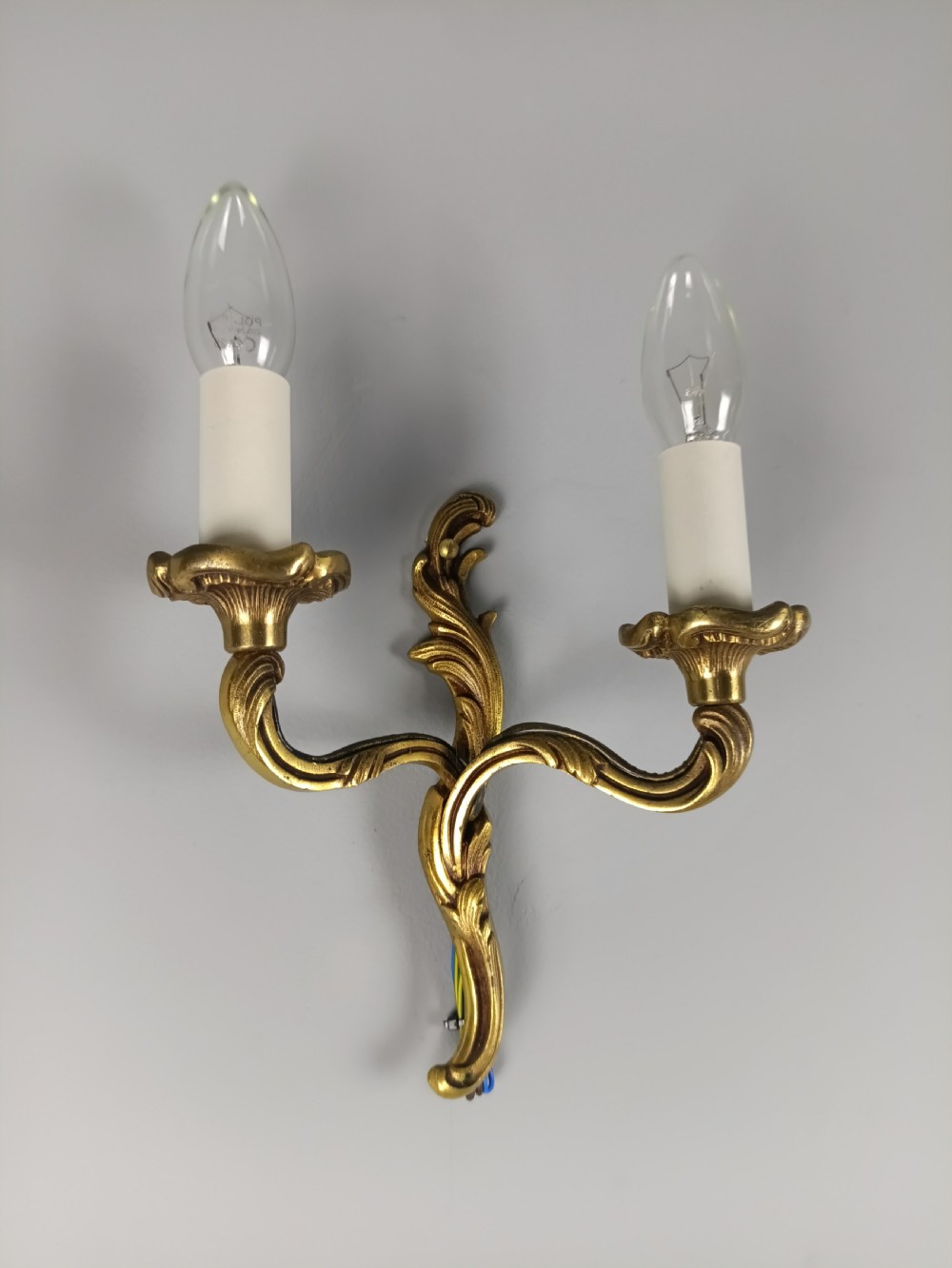 An antique French twin-arm gilt brass wall light featuring cast acanthus leaf scrolling and faux candle sleeves. View II