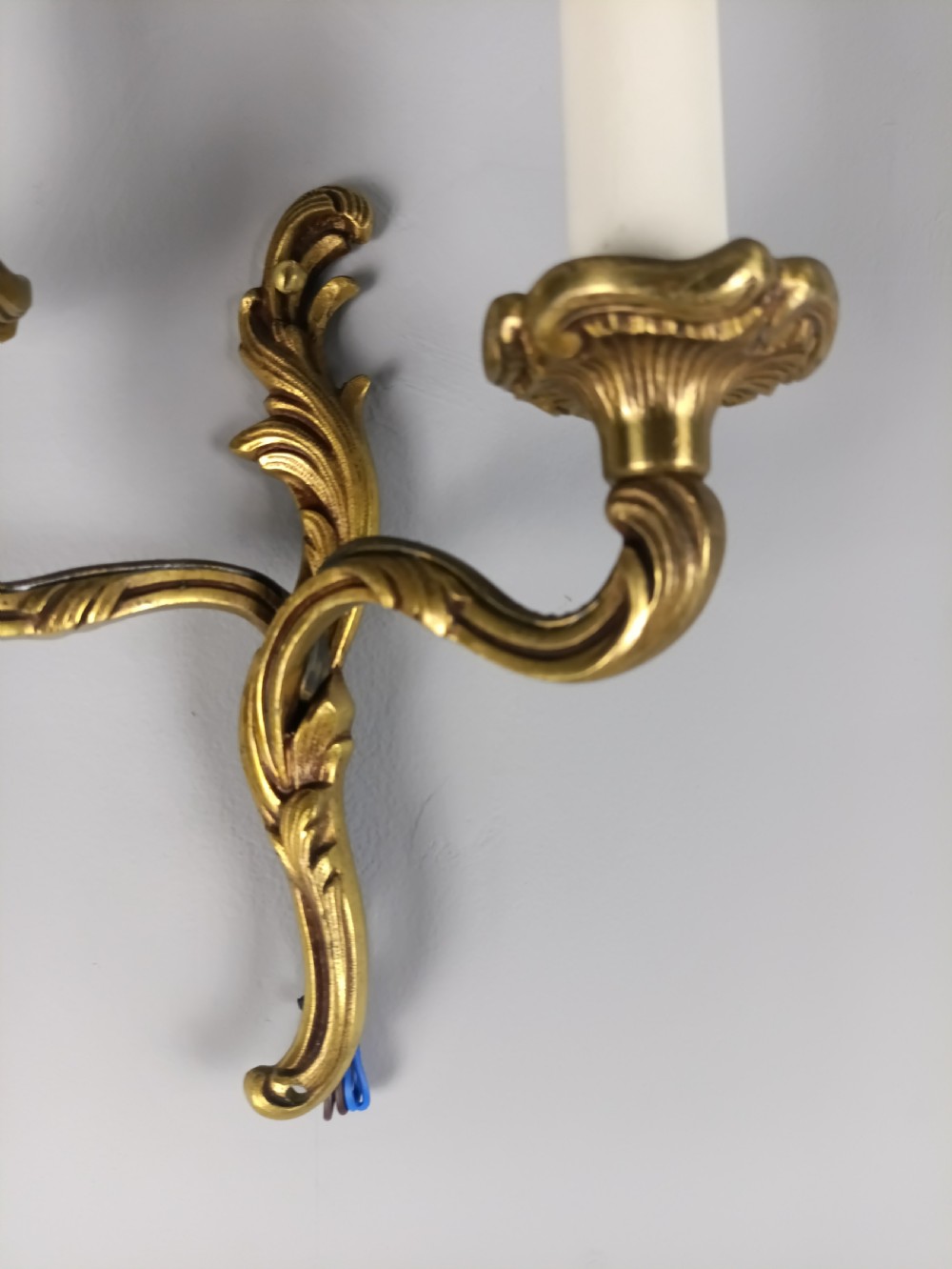 An antique French twin-arm gilt brass wall light featuring cast acanthus leaf scrolling and faux candle sleeves. View III