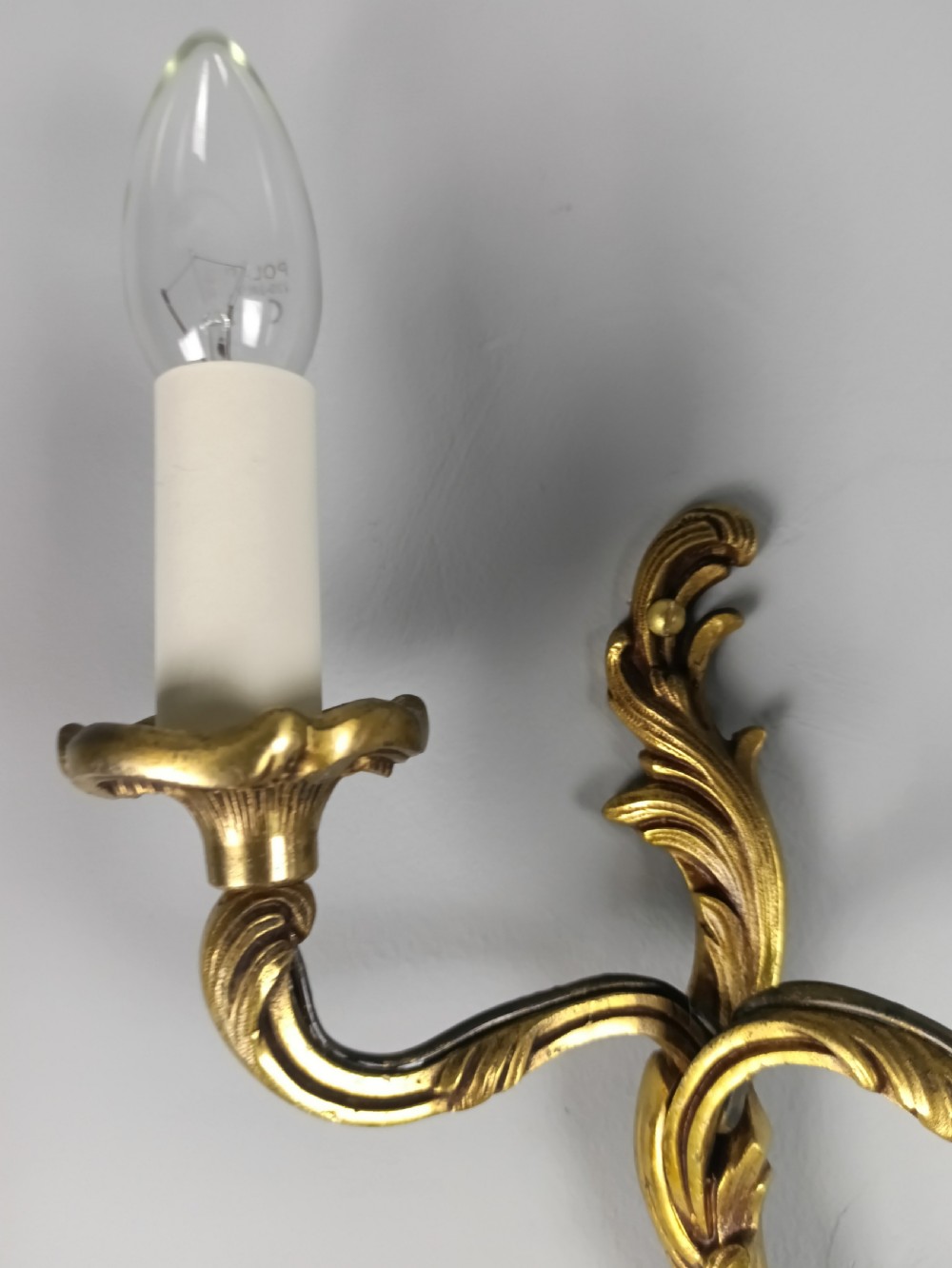 An antique French twin-arm gilt brass wall light featuring cast acanthus leaf scrolling and faux candle sleeves. View IV