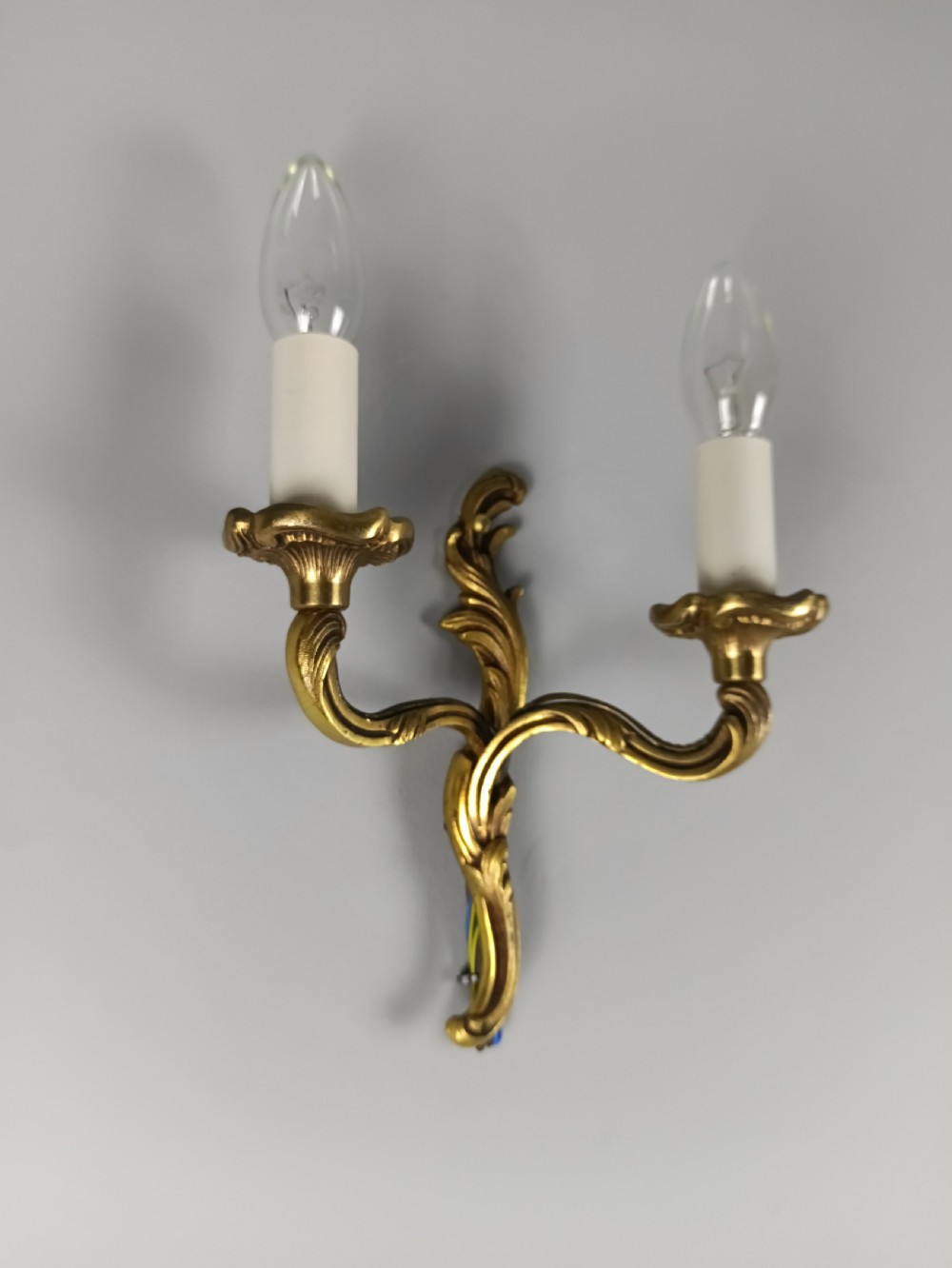 An antique French twin-arm gilt brass wall light featuring cast acanthus leaf scrolling and faux candle sleeves. View V