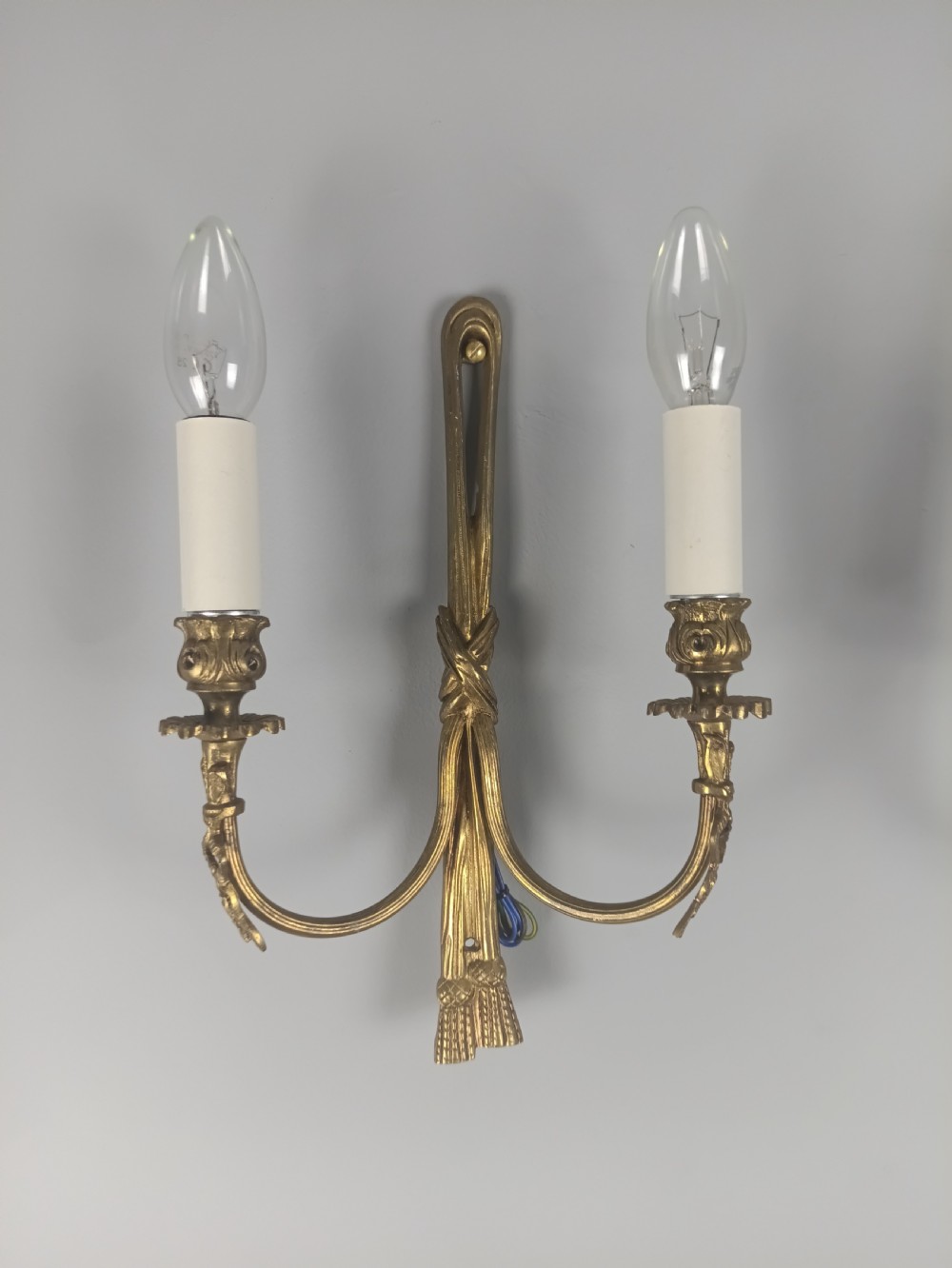 A pair of antique French gilt brass wall sconces featuring ribbon bow top motifs, tassel backplates, and twin candle arms. View II