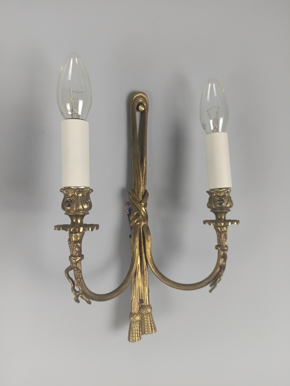 A pair of antique French gilt brass wall sconces featuring ribbon bow top motifs, tassel backplates, and twin candle arms. View III