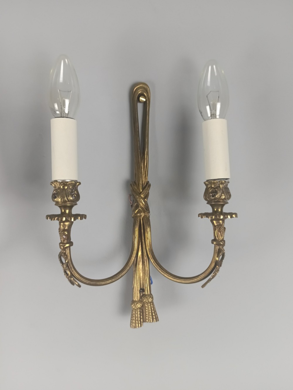 A pair of antique French gilt brass wall sconces featuring ribbon bow top motifs, tassel backplates, and twin candle arms. View IV