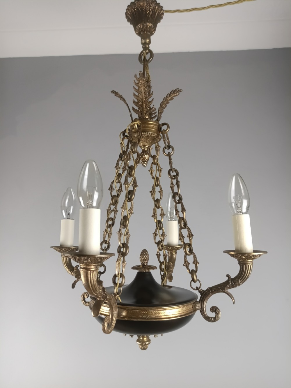 A French Empire four-light chandelier with a dark patinated central bowl suspended by decorative brass chains and acanthus leaf motifs.