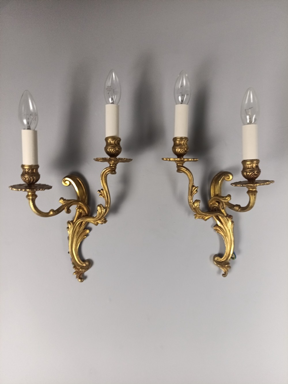 A pair of French gilt brass two-arm wall sconces featuring scrolling acanthus leaf details and candle-style bulb holders.