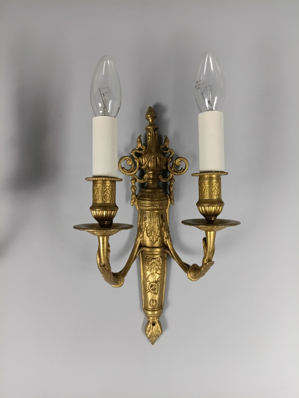 A pair of 19th-century French gilt brass twin-arm wall sconces featuring urn-topped backplates and classical foliage relief work. View II