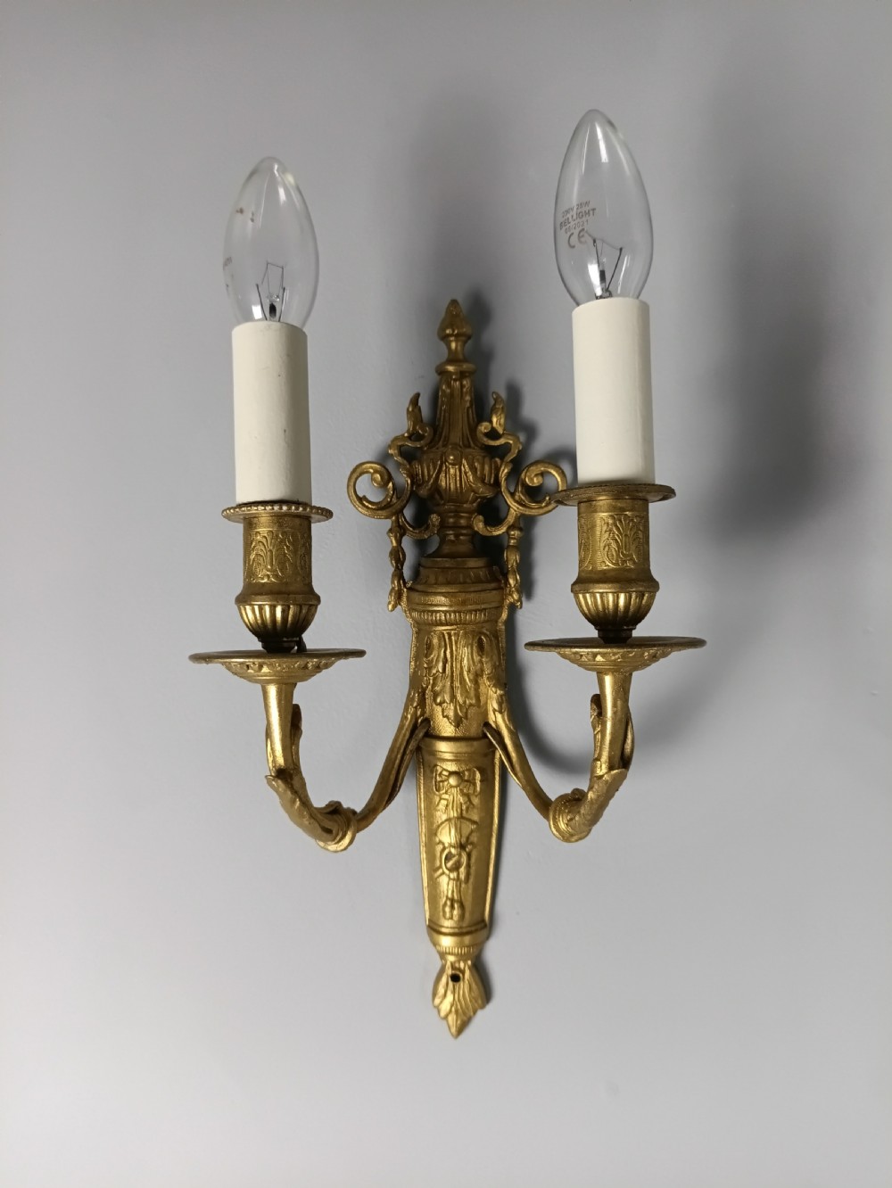 A pair of 19th-century French gilt brass twin-arm wall sconces featuring urn-topped backplates and classical foliage relief work. View III