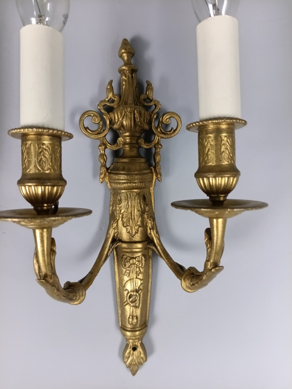 A pair of 19th-century French gilt brass twin-arm wall sconces featuring urn-topped backplates and classical foliage relief work. View IV