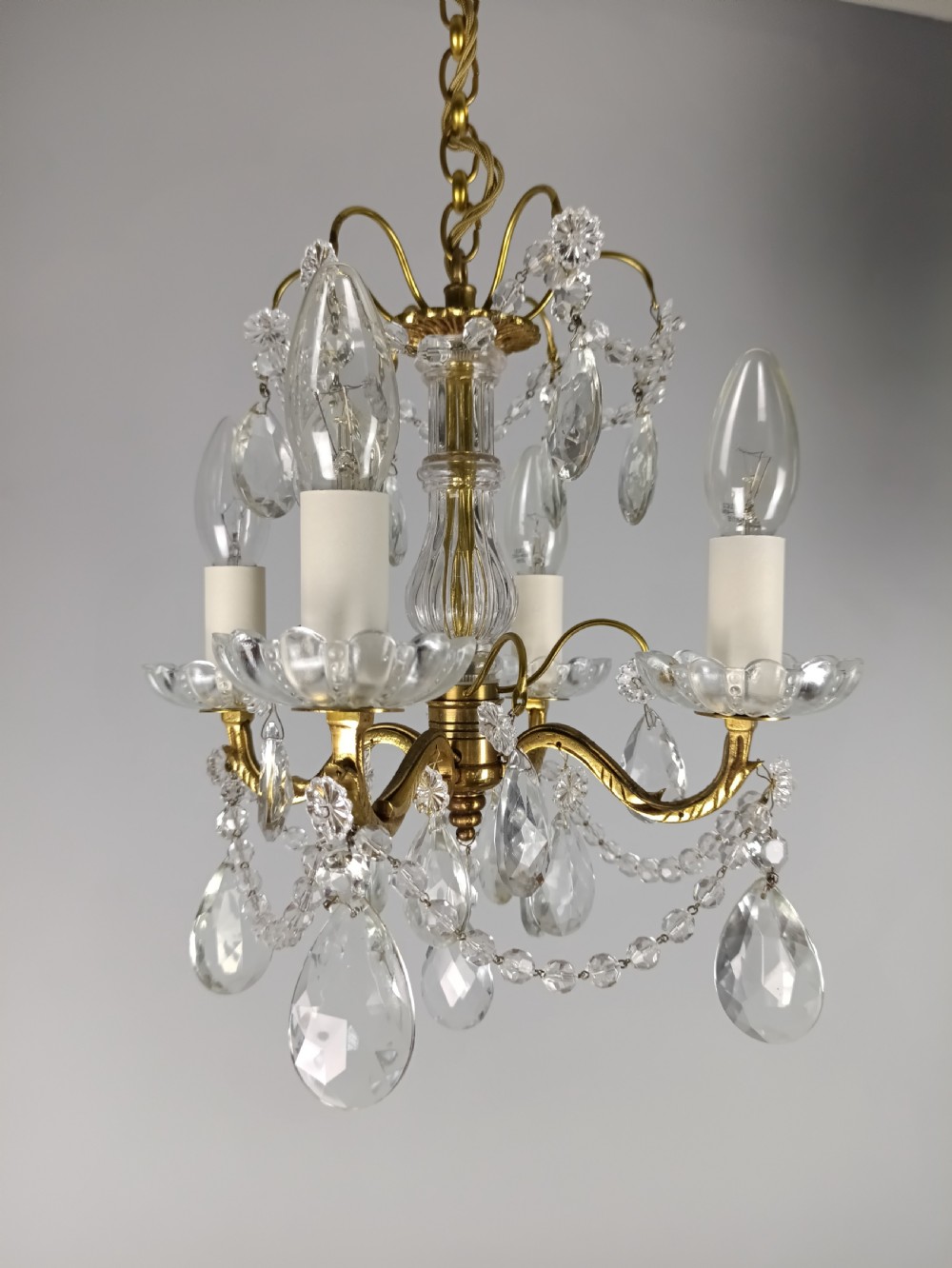 A small French brass four-light chandelier adorned with clear cut-crystal droplets, faceted glass swags, and scalloped glass drip pans.