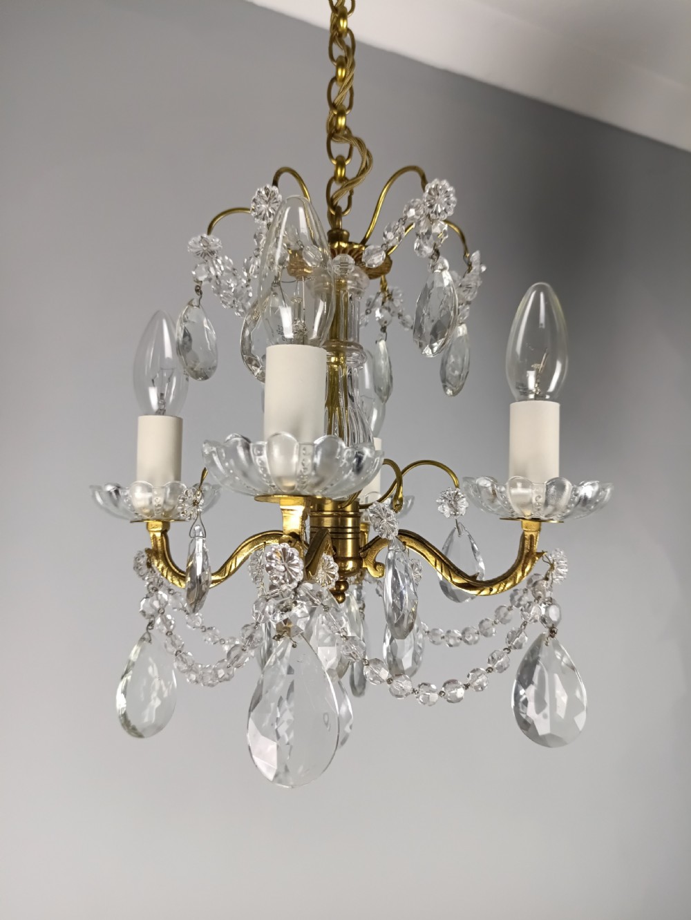 A small French brass four-light chandelier adorned with clear cut-crystal droplets, faceted glass swags, and scalloped glass drip pans. View II
