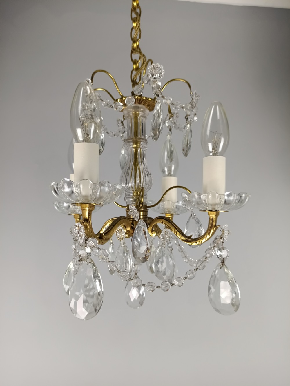 A small French brass four-light chandelier adorned with clear cut-crystal droplets, faceted glass swags, and scalloped glass drip pans. View III