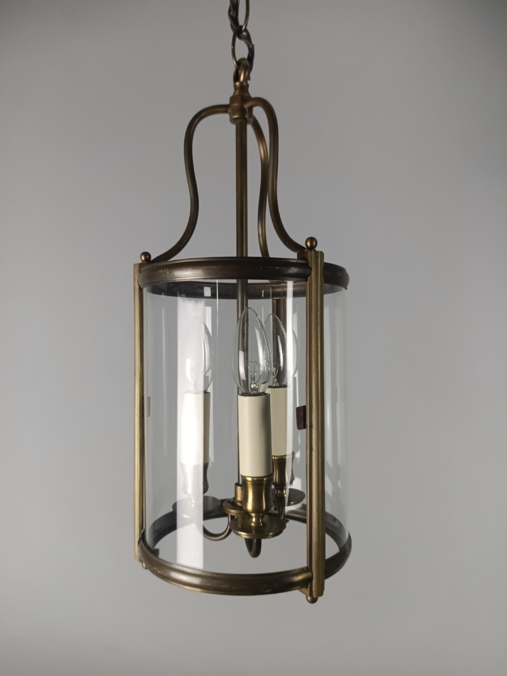 A cylindrical gilded brass hall lantern featuring curved clear glass panels and an internal three-light candle cluster.