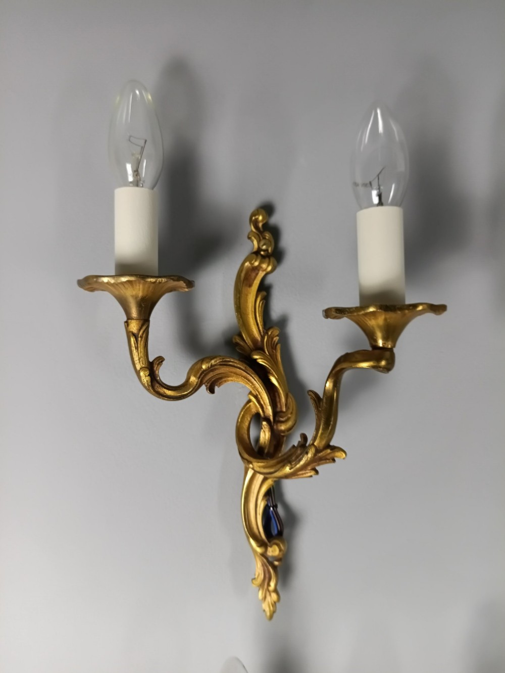Four French Rococo style gilded bronze twin-arm wall lights with foliate scrollwork and white candle sleeves. View II