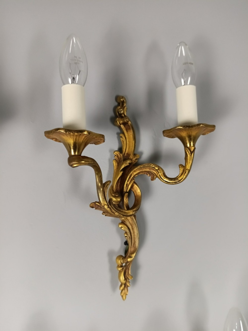 Four French Rococo style gilded bronze twin-arm wall lights with foliate scrollwork and white candle sleeves. View III