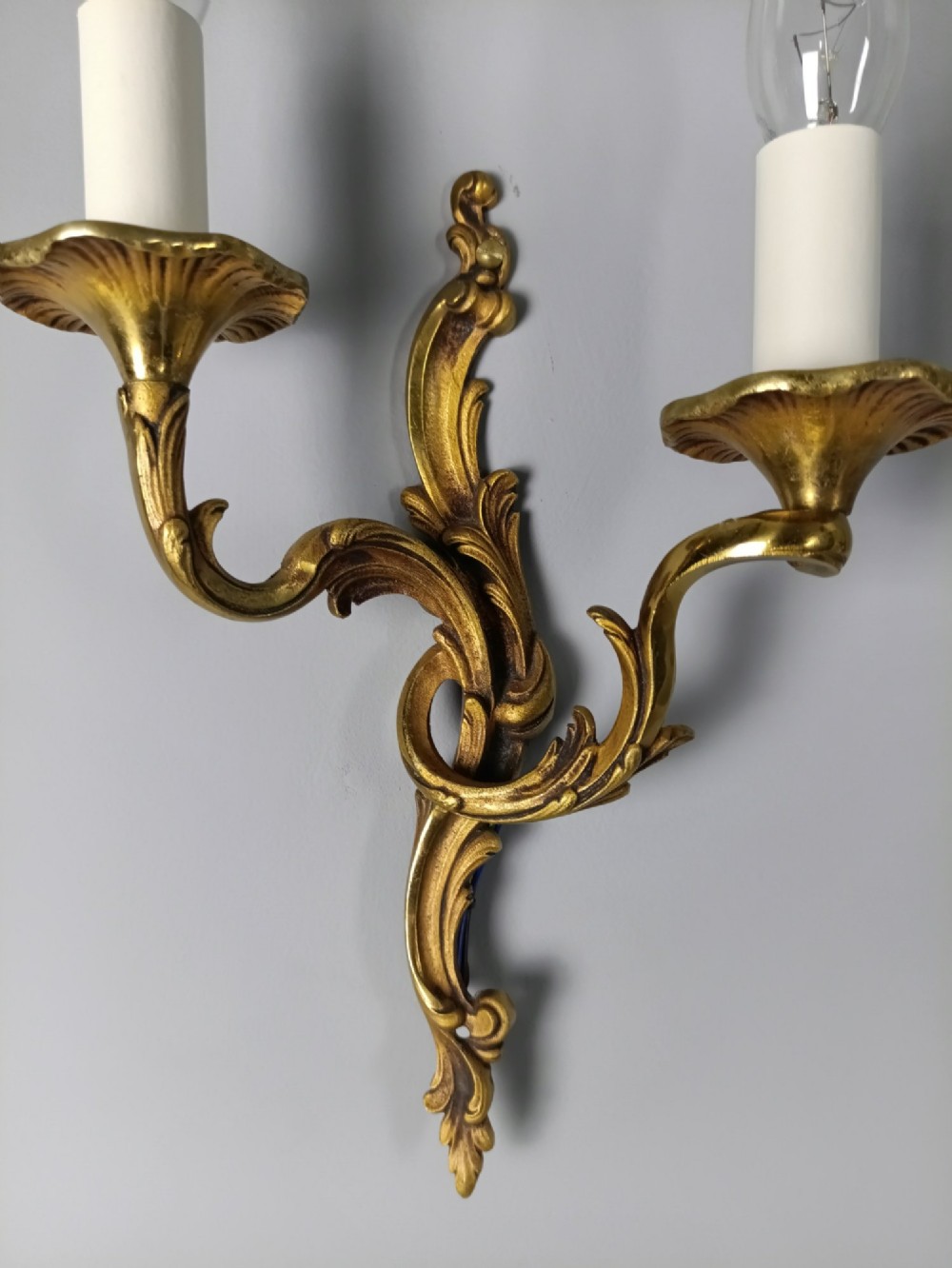 Four French Rococo style gilded bronze twin-arm wall lights with foliate scrollwork and white candle sleeves. View VI