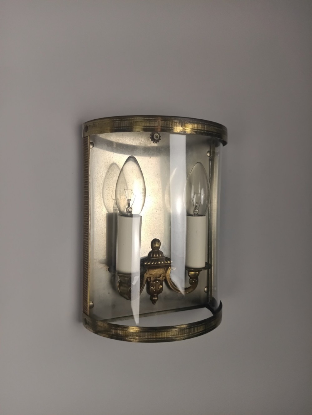A pair of French gilt brass half-lantern wall lights featuring curved clear glass panels and twin candle-style sockets. View V