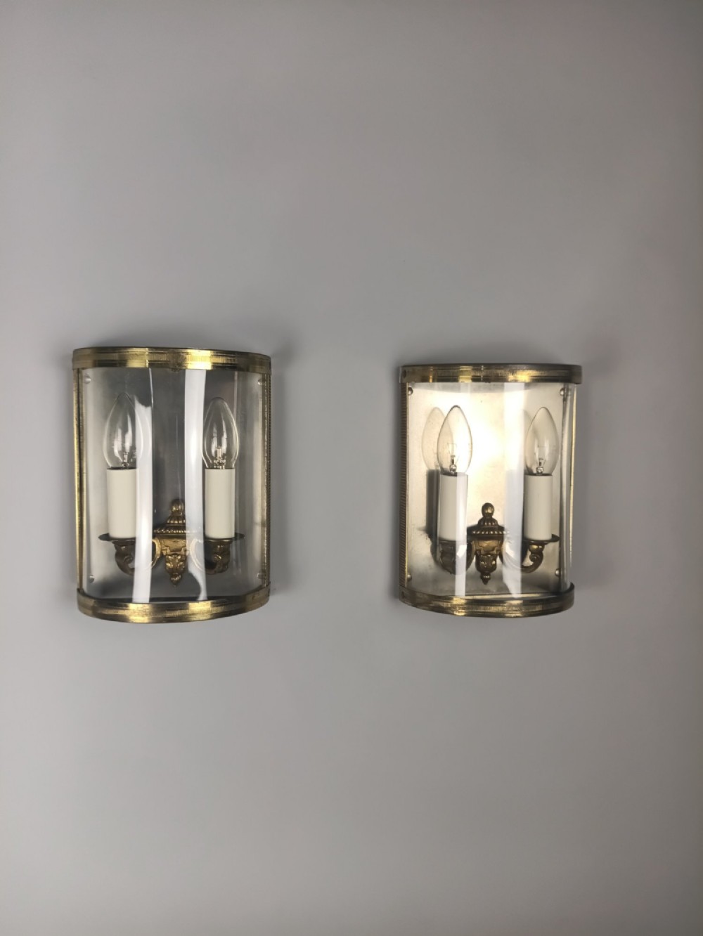 A pair of French gilt brass half-lantern wall lights featuring curved clear glass panels and twin candle-style sockets. View IX