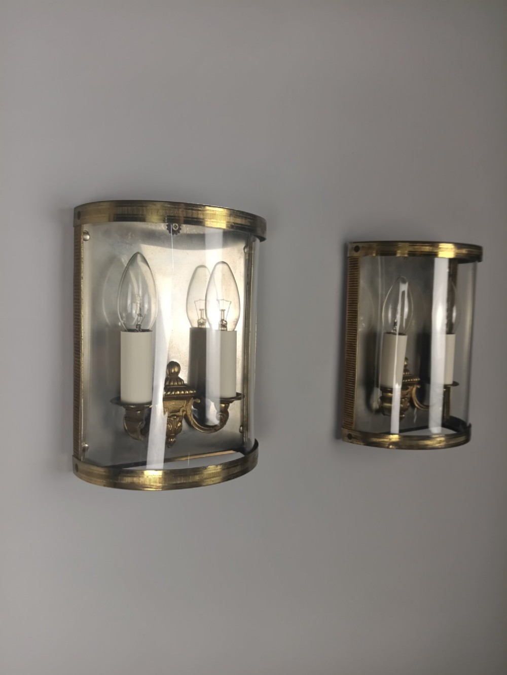 A pair of French gilt brass half-lantern wall lights featuring curved clear glass panels and twin candle-style sockets. View X