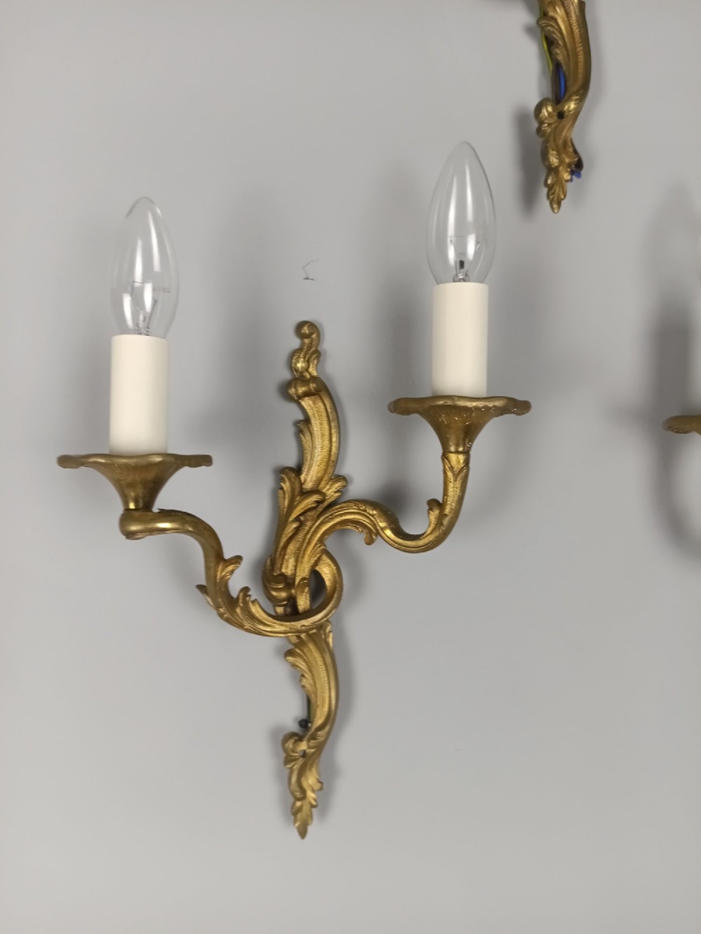A set of three French gilded bronze twin-arm wall lights with ornate foliage scrolling and candle-style sockets. View III