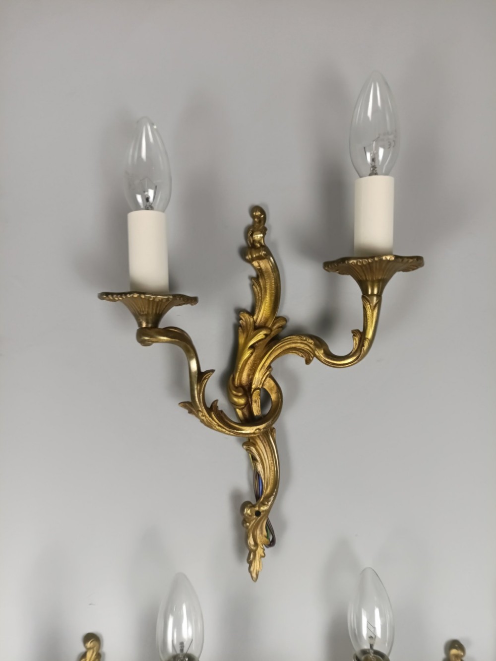 A set of three French gilded bronze twin-arm wall lights with ornate foliage scrolling and candle-style sockets. View V
