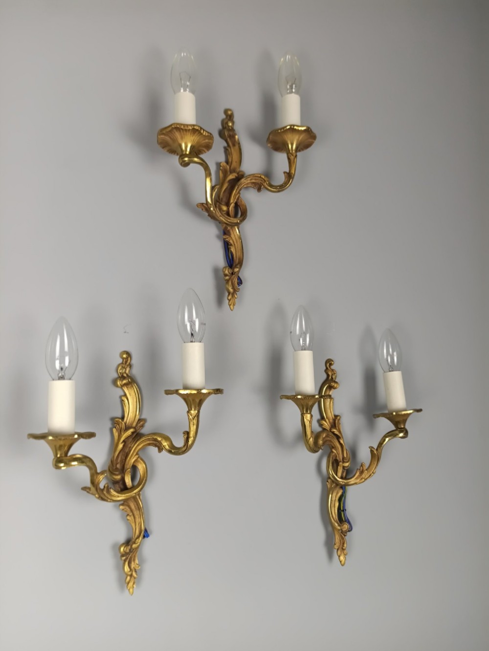 Set of three French Rococo style gilt bronze wall sconces featuring twin sweeping arms, foliate scroll backplates, and candle-effect fittings. View II