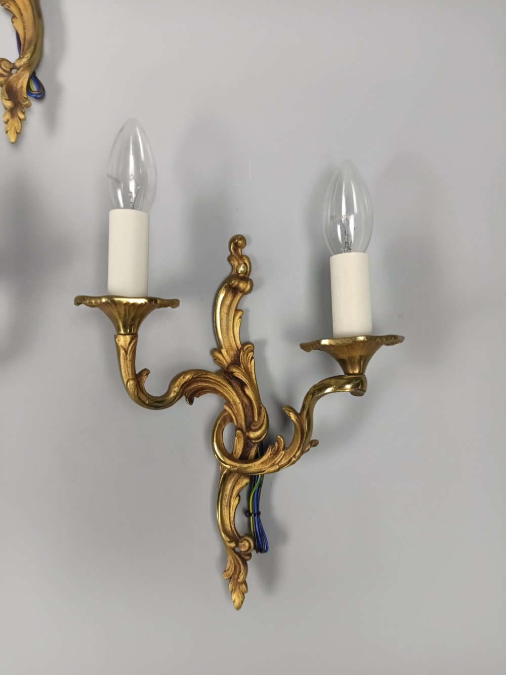 Set of three French Rococo style gilt bronze wall sconces featuring twin sweeping arms, foliate scroll backplates, and candle-effect fittings. View IV