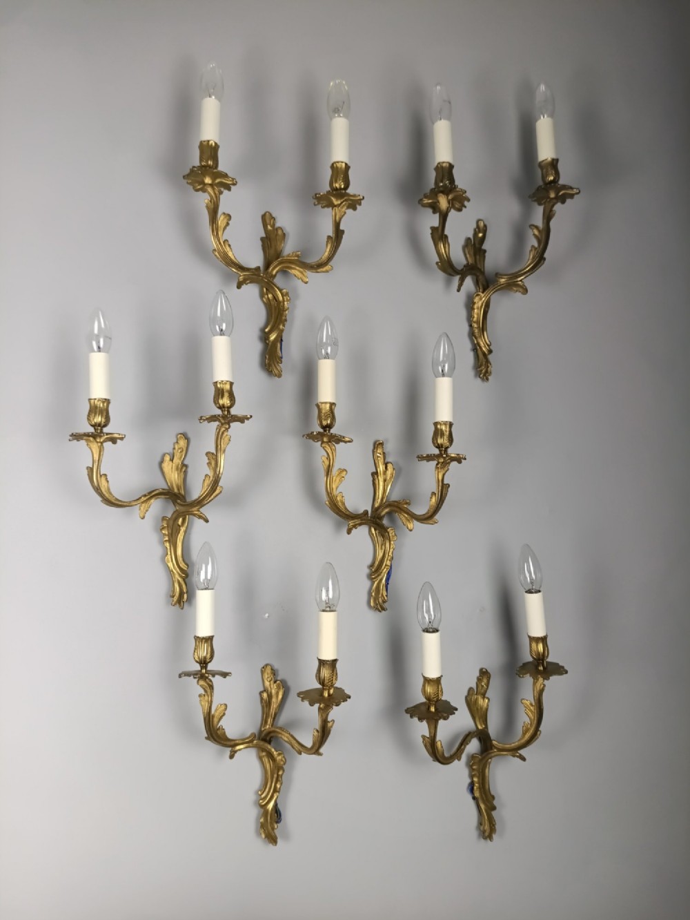 A set of six French Rococo style twin-arm gilded brass wall lights featuring acanthus leaf scrollwork and white candle sleeves. View II