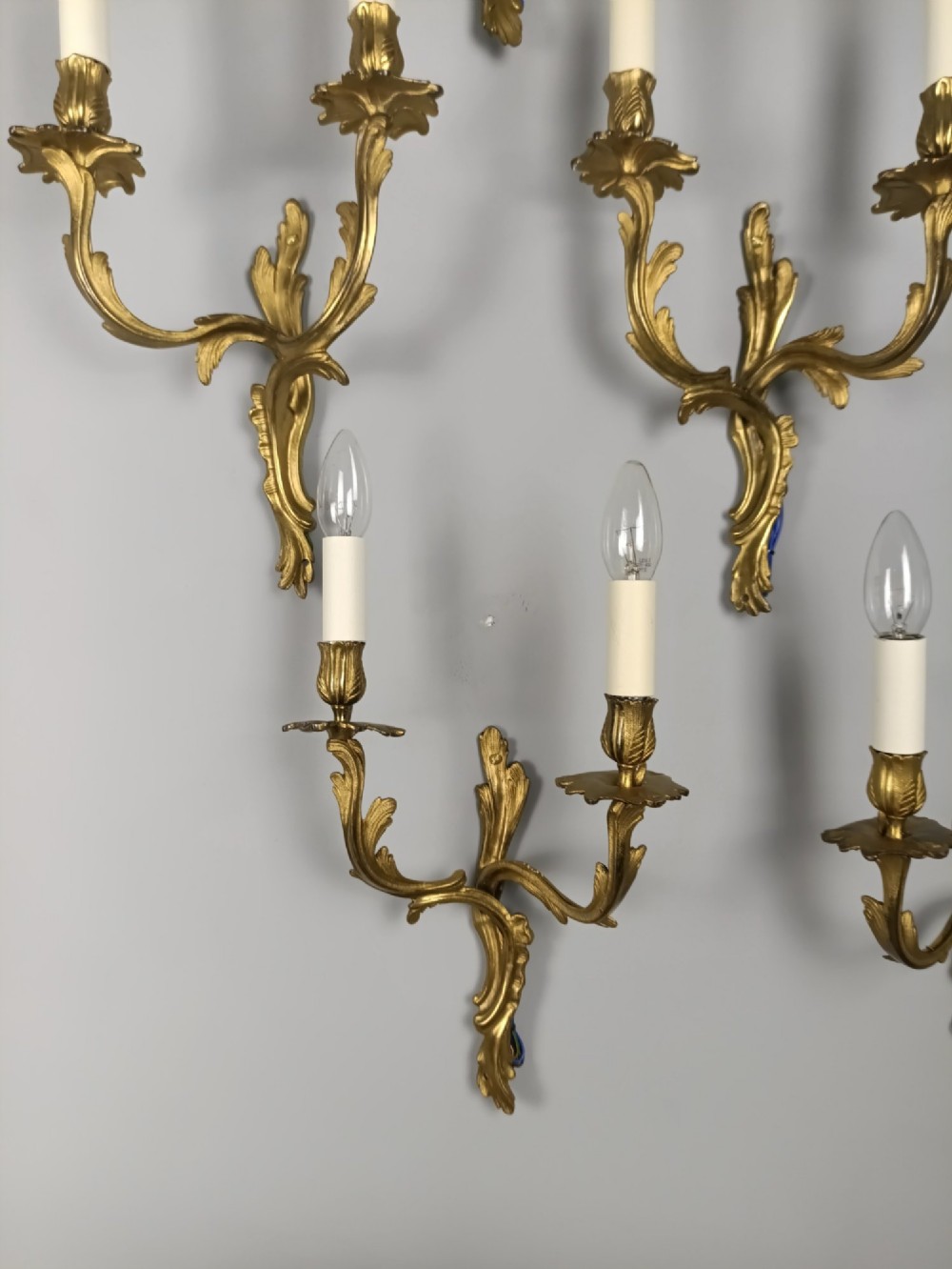 A set of six French Rococo style twin-arm gilded brass wall lights featuring acanthus leaf scrollwork and white candle sleeves. View VII