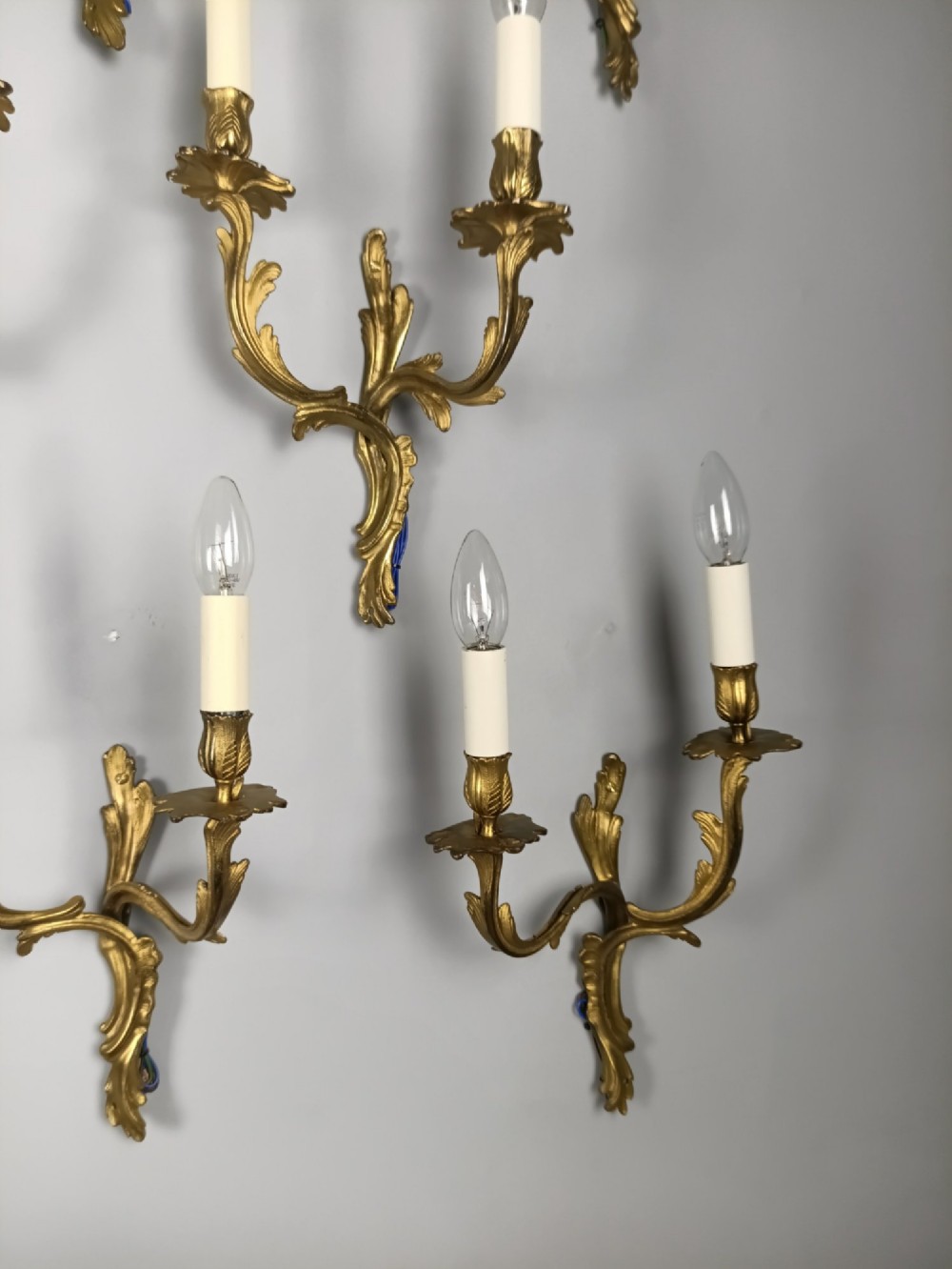 A set of six French Rococo style twin-arm gilded brass wall lights featuring acanthus leaf scrollwork and white candle sleeves. View VIII