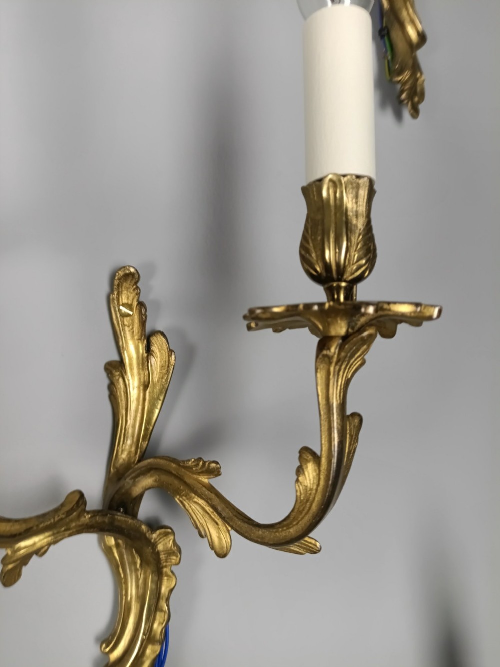 A set of six French Rococo style twin-arm gilded brass wall lights featuring acanthus leaf scrollwork and white candle sleeves. View X