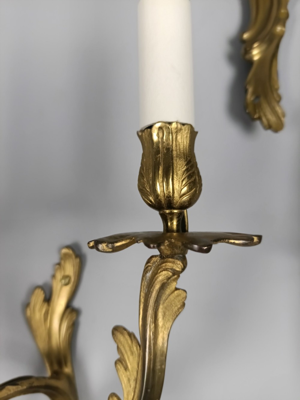 A set of six French Rococo style twin-arm gilded brass wall lights featuring acanthus leaf scrollwork and white candle sleeves. View XI