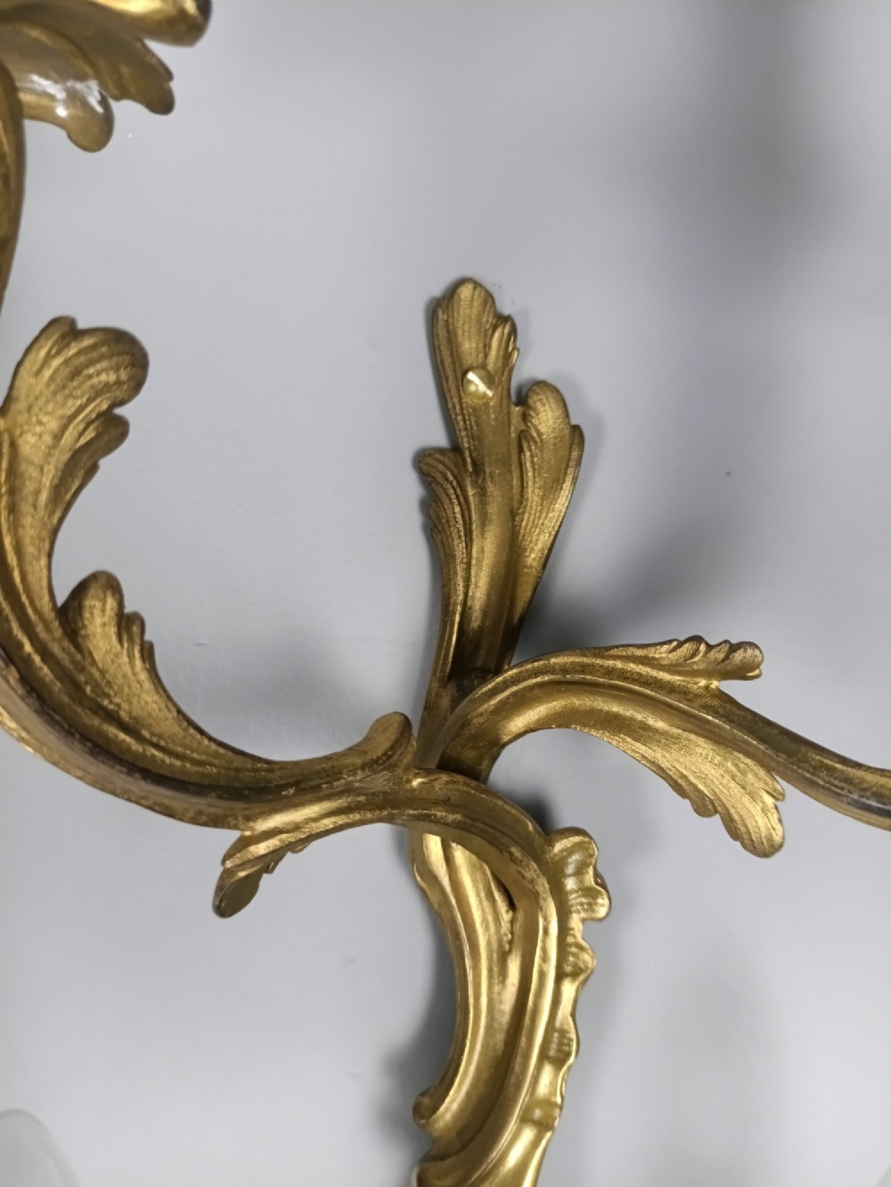 A set of six French Rococo style twin-arm gilded brass wall lights featuring acanthus leaf scrollwork and white candle sleeves. View XII