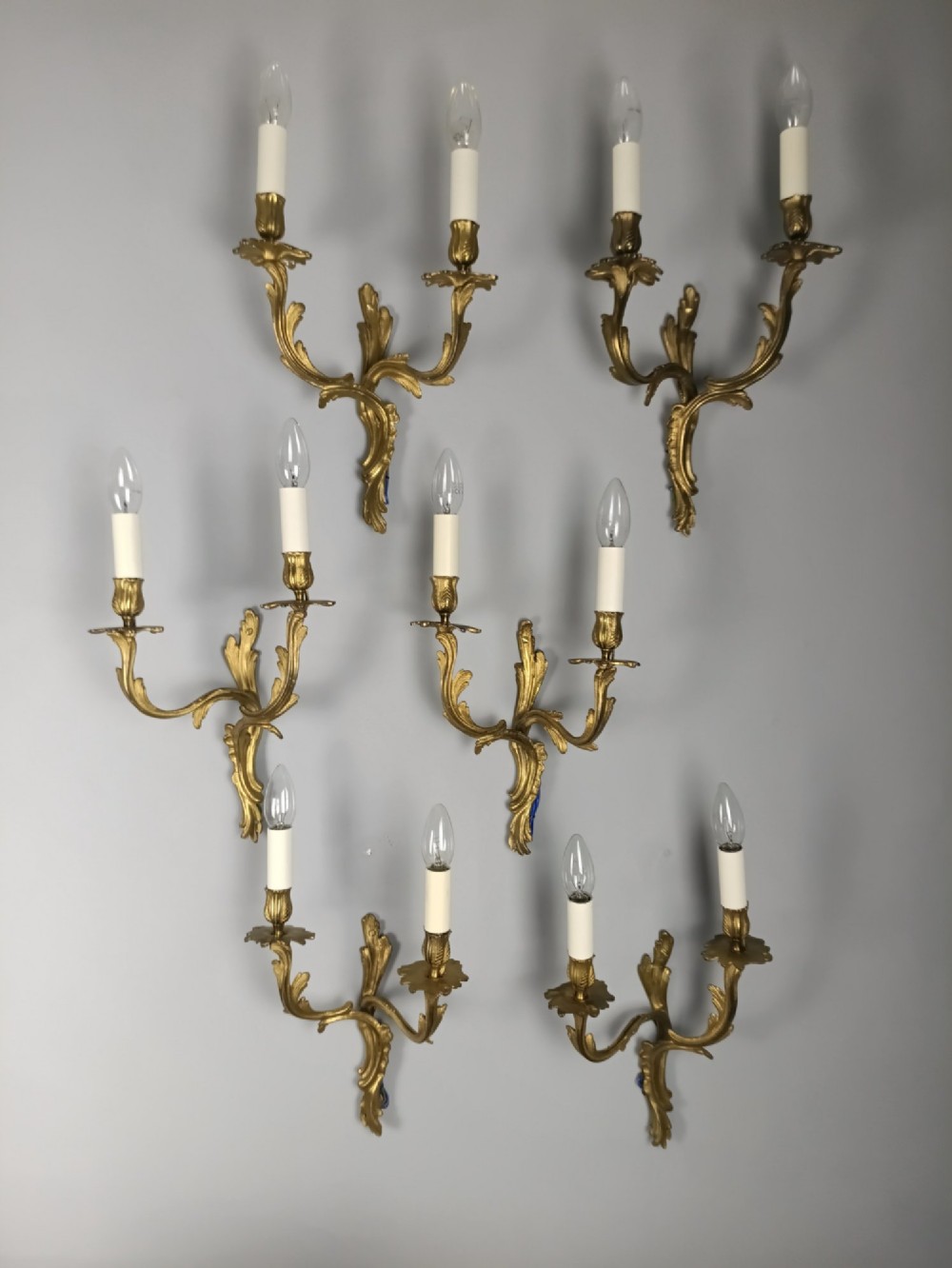 A set of six French Rococo style twin-arm gilded brass wall lights featuring acanthus leaf scrollwork and white candle sleeves. View XIII