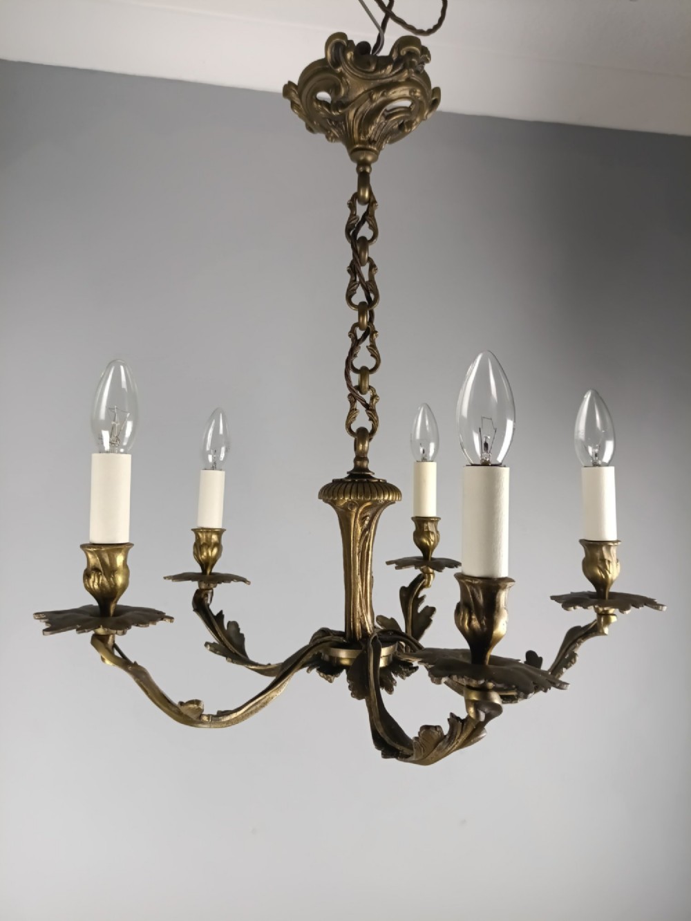 A five-arm dark bronze chandelier with cast acanthus leaf arms, white candle sleeves, and a matching hanging chain with ceiling rose. View II