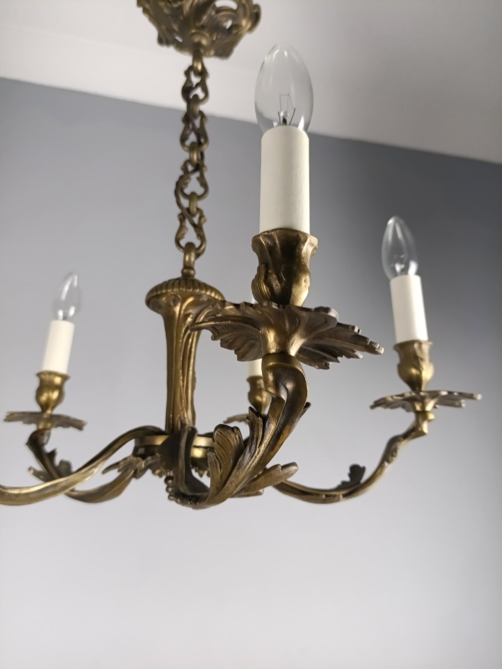 A five-arm dark bronze chandelier with cast acanthus leaf arms, white candle sleeves, and a matching hanging chain with ceiling rose. View IV