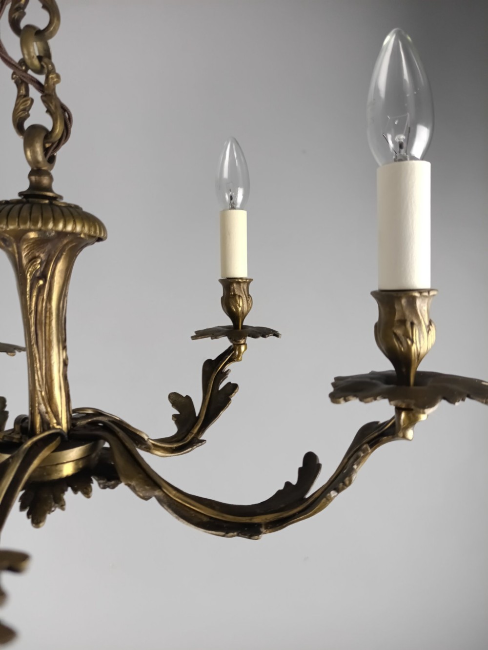 A five-arm dark bronze chandelier with cast acanthus leaf arms, white candle sleeves, and a matching hanging chain with ceiling rose. View V