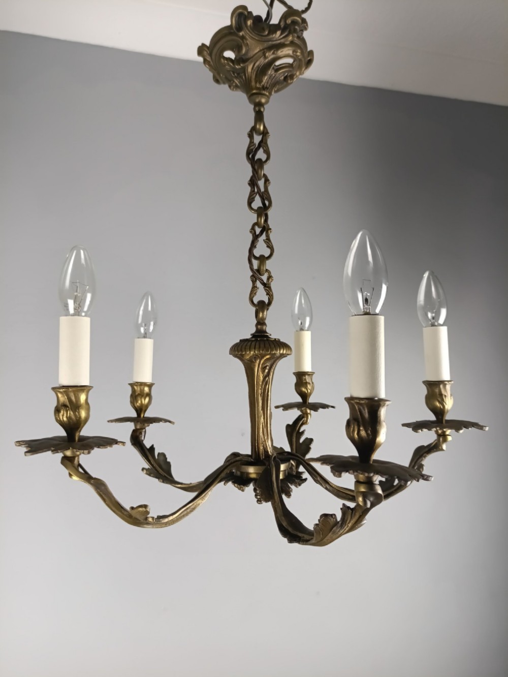 A five-arm dark bronze chandelier with cast acanthus leaf arms, white candle sleeves, and a matching hanging chain with ceiling rose. View VII