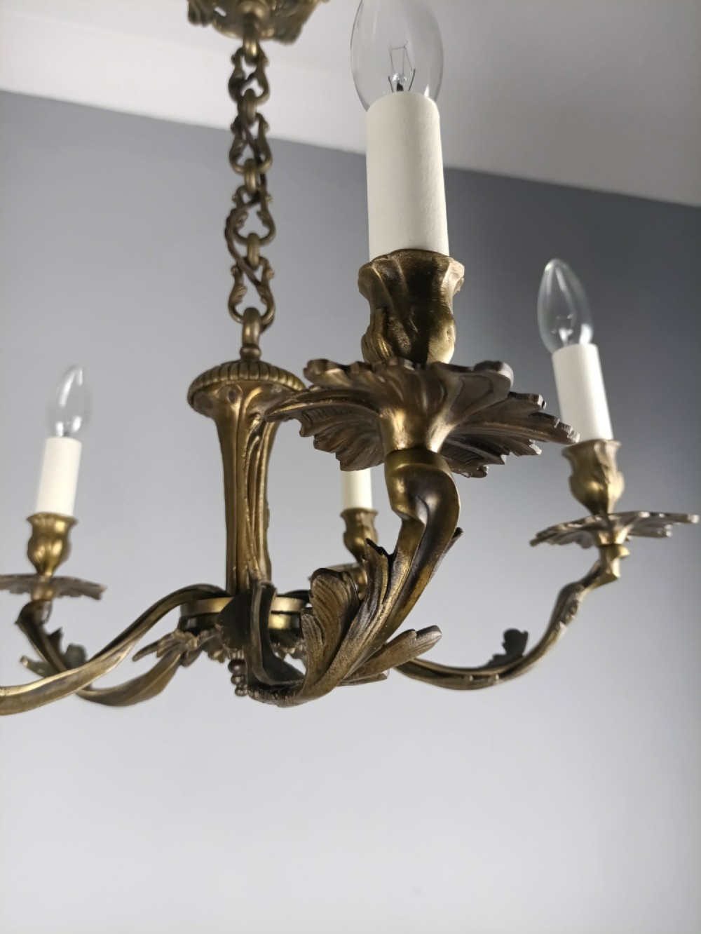 A five-arm dark bronze chandelier with cast acanthus leaf arms, white candle sleeves, and a matching hanging chain with ceiling rose. View IX