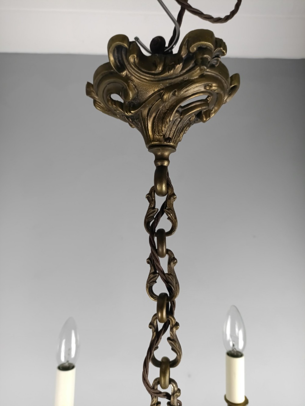 A five-arm dark bronze chandelier with cast acanthus leaf arms, white candle sleeves, and a matching hanging chain with ceiling rose. View X